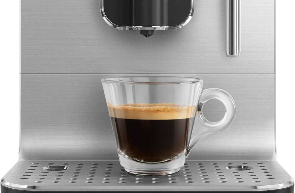 Na obrazie widoczny jest ekspres do kawy z filiżanką espresso na metalowej tacce ociekowej. Ekspres ma srebrną obudowę i dyszę do spieniania mleka.