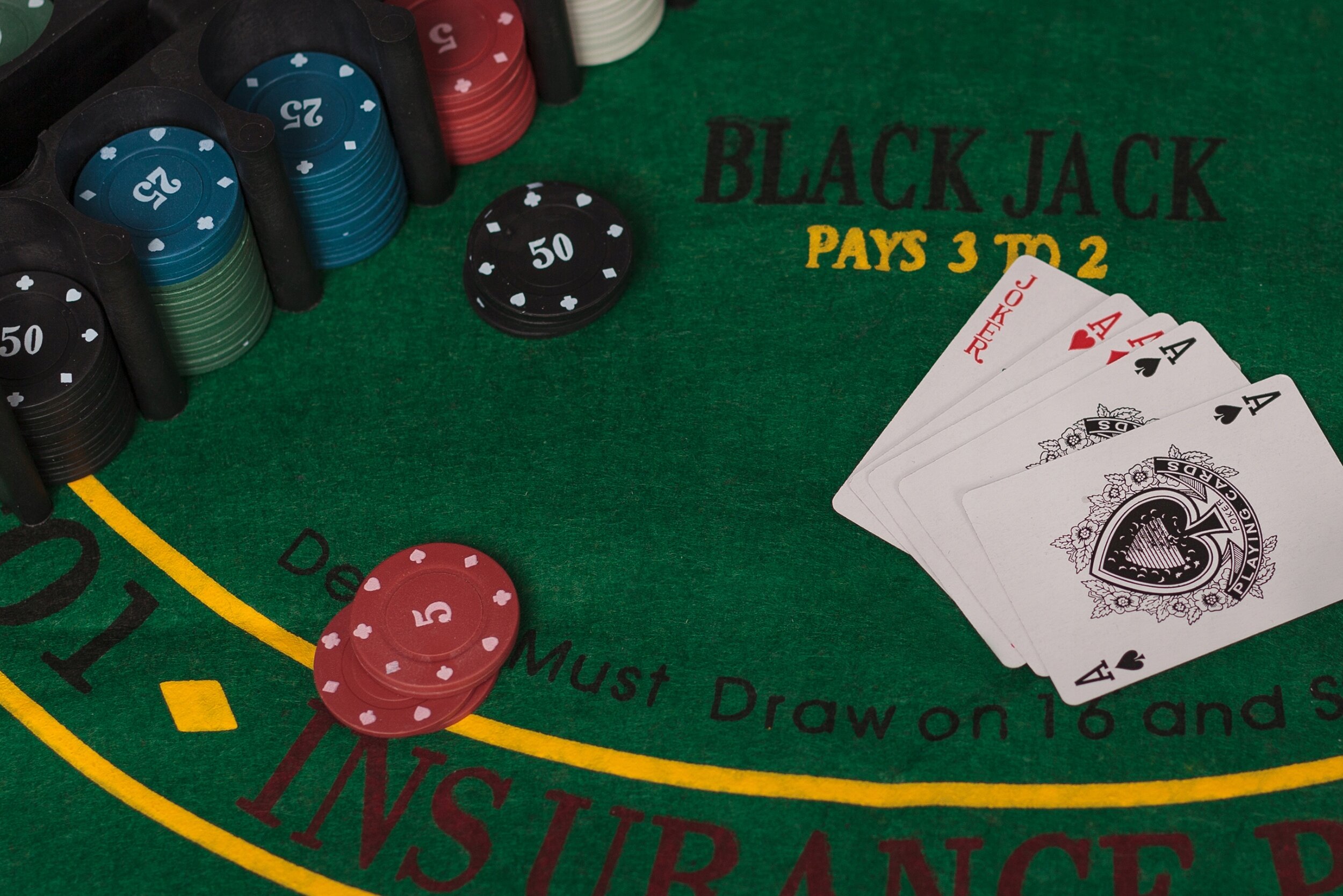 Na zielonym stole do gry w blackjacka leżą karty i żetony o różnych nominałach. Widoczny jest napis \'BLACK JACK PAYS 3 TO 2\'.