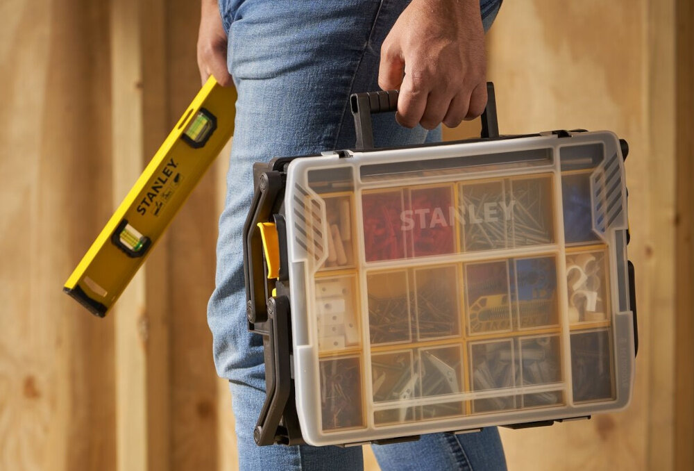 Organizer STANLEY STST1-75540 osoba trzyma organizer w dłoni w tle drewniana ściana zintegrowany uchwyt ergonomiczna forma waga 1,8 kg
