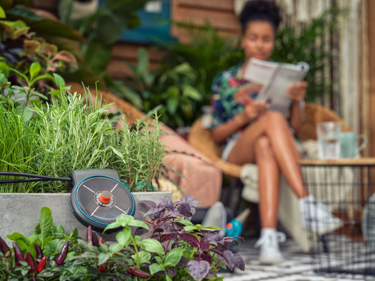 Zestaw do nawadniania GARDENA Micro-Drip-System 13000-20 (10 m), balkony, rozdzielacze, podłoże, litry, gleba, kobieta w tle czyta książkę, na pierwszym planie zestaw do nawadniania