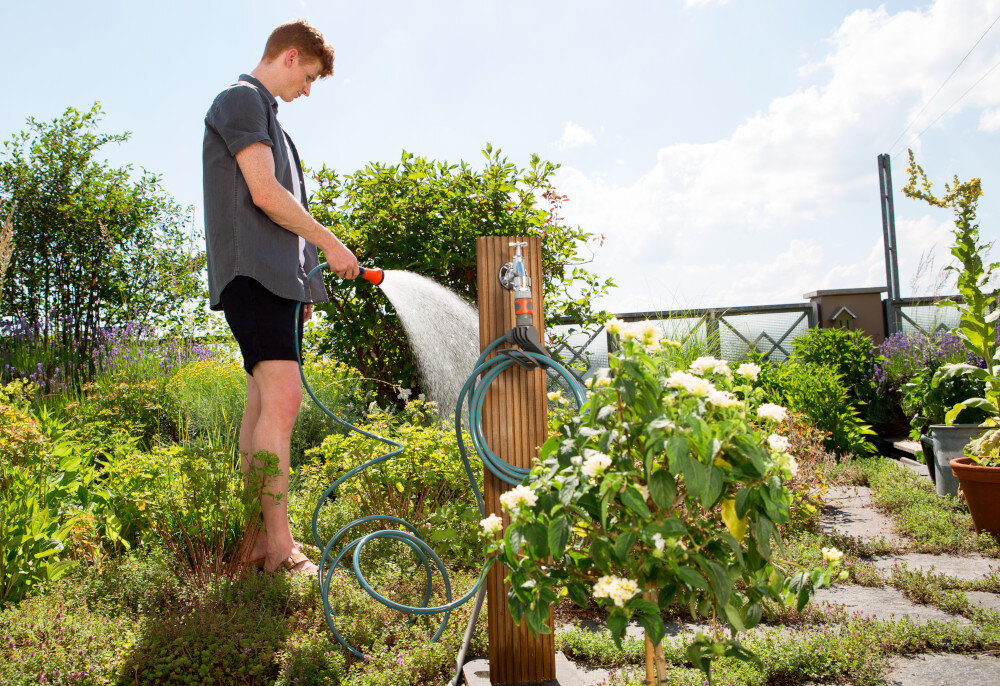 Zestaw GARDENA City Gardening wąż spiralny zraszacz natrysk 3/8 cala 7.5 m 18411-20 ogród słupek na słupku wąż osoba podlewa rośliny w ogrodzie w tle niebo wygodne nawadnianie do niewielkich przestrzeni zestaw gotowy do użycia