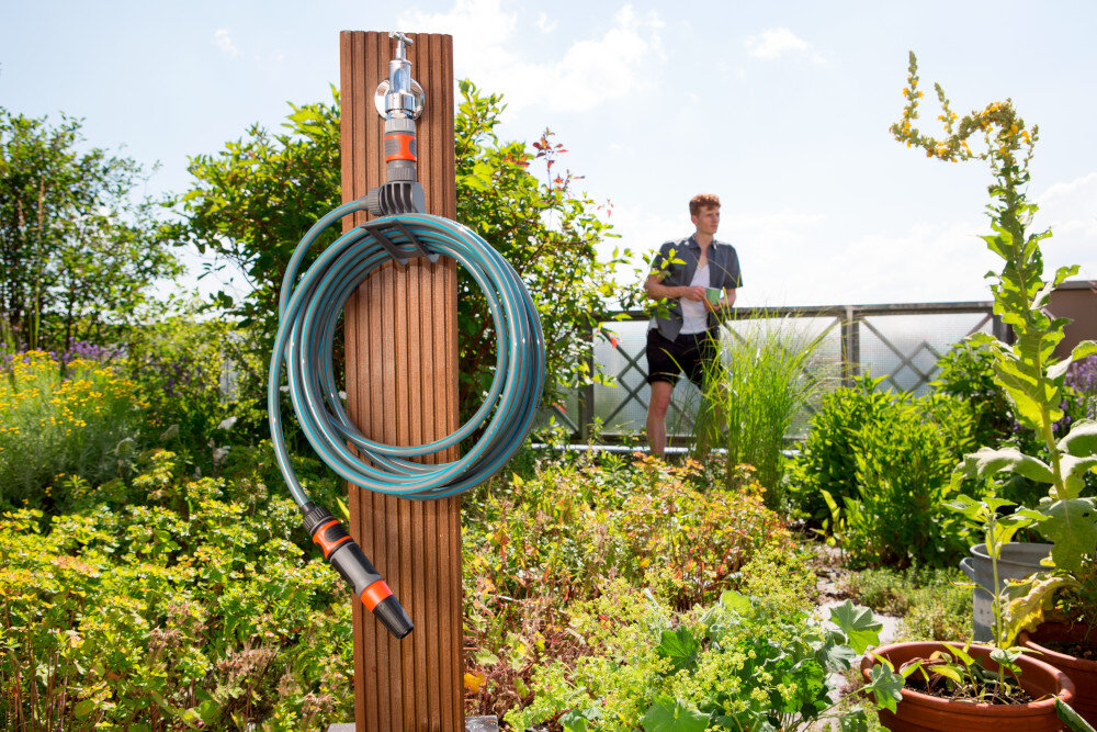 Zestaw GARDENA City Gardening wąż spiralny zraszacz prosty 3/8 cala 7.5 m 18401-20 ogród słupek zwinięty wąż i zraszacz umieszczony na słupku w tle stoi osoba wbudowany wieszak przechowywanie węża w uporządkowany sposób montaż nie wymaga skomplikowanych narzędzi w każdej chwili można go zawiesić lub zdjąć