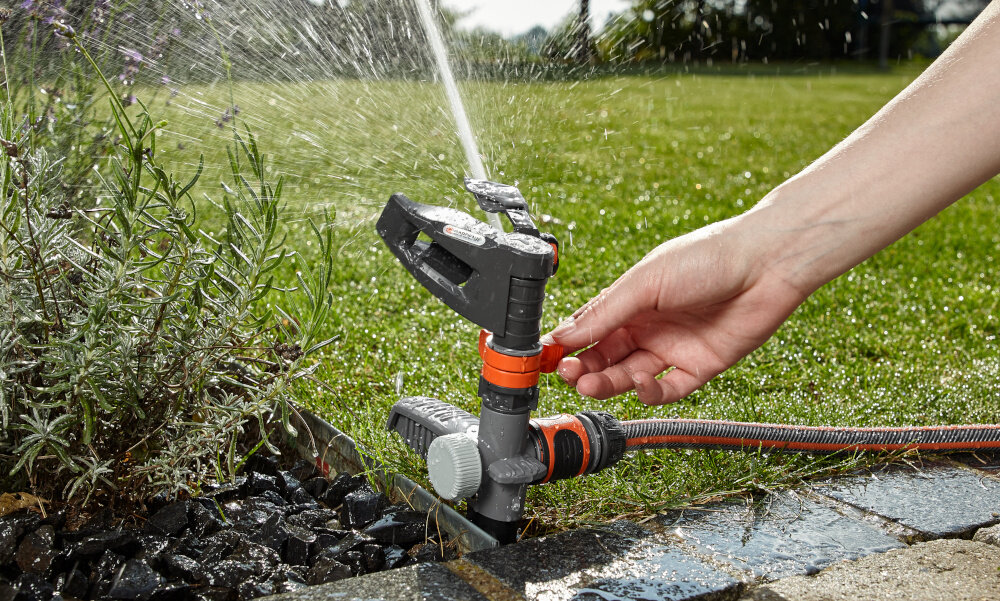 Zraszacz GARDENA 8137-20 ogród trawnik chodnik osoba trzyma w palcach pokrętło do regulacji zasięg w zakresie od 5 do 12,5 metra dopasowanie pracy do wielkości ogrodu skuteczne nawadnianie