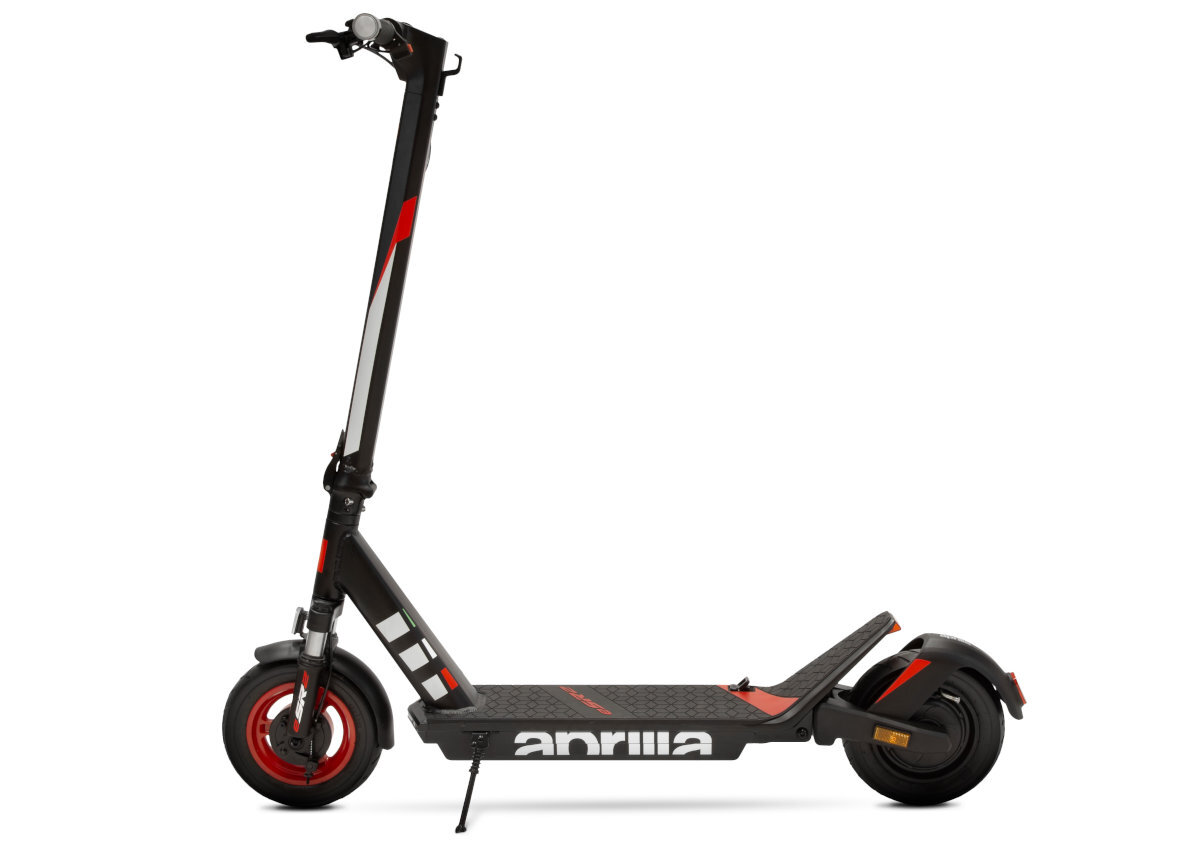 Czarno-czerwona hulajnoga elektryczna z widocznym logo \'aprilia\' na podeście. Posiada duże koła i dwa amortyzatory.