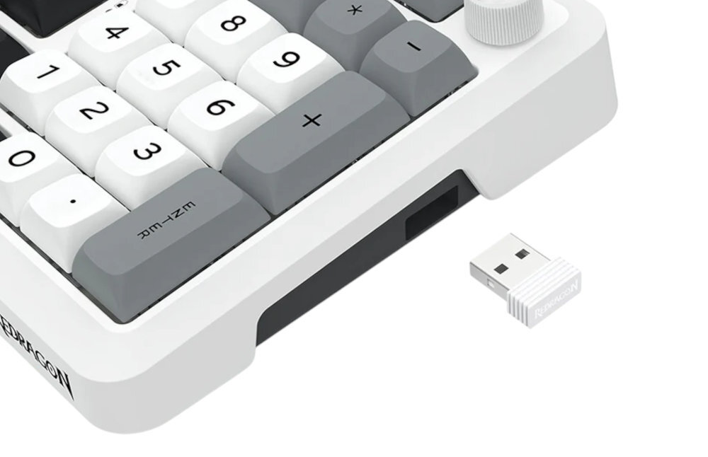 Fragment klawiatury numerycznej z białymi i szarymi klawiszami oraz widocznym logo \'REDRAGON\'. Obok klawiatury znajduje się biały adapter USB.