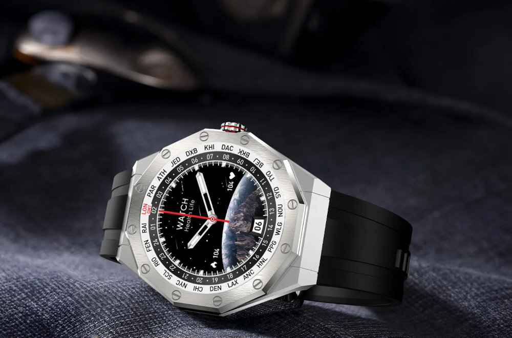 Srebrny smartwatch z czarnym paskiem leży na ciemnym materiale. Na tarczy widoczny jest napis \'WATCH\' oraz data \'30\'.
