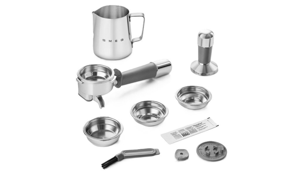 Na obrazie widoczne są akcesoria do ekspresu do kawy, w tym metalowy dzbanek z napisem \'SMEG\', uchwyt na portafilter, tamper, sitka, szczotka oraz inne drobne elementy.