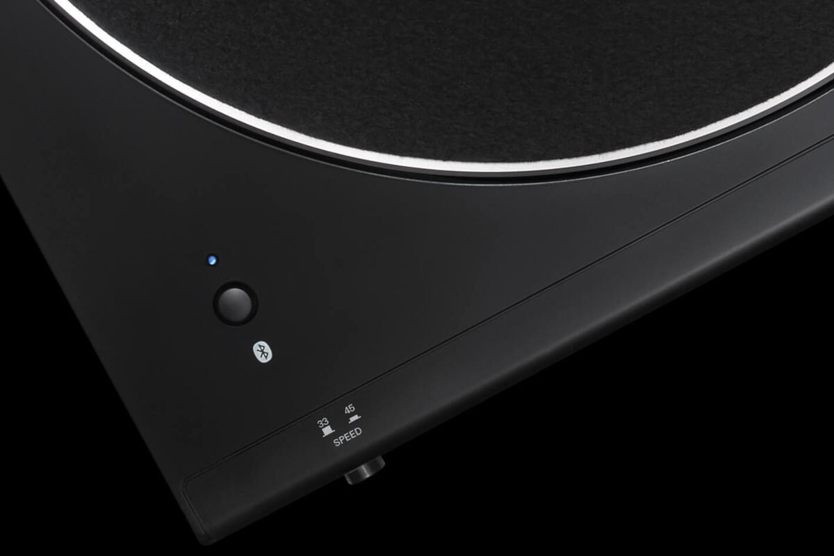 Czarny gramofon z widocznym przyciskiem Bluetooth i niebieską diodą. Obok znajduje się oznaczenie prędkości \'33\' i \'45\' oraz napis \'SPEED\'.
