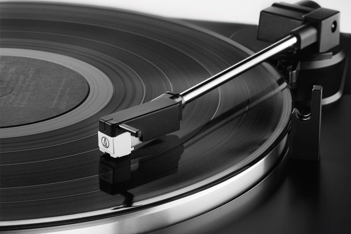 Czarny gramofon z widocznym ramieniem i igłą na płycie winylowej. Na igle znajduje się logo Audio-Technica.