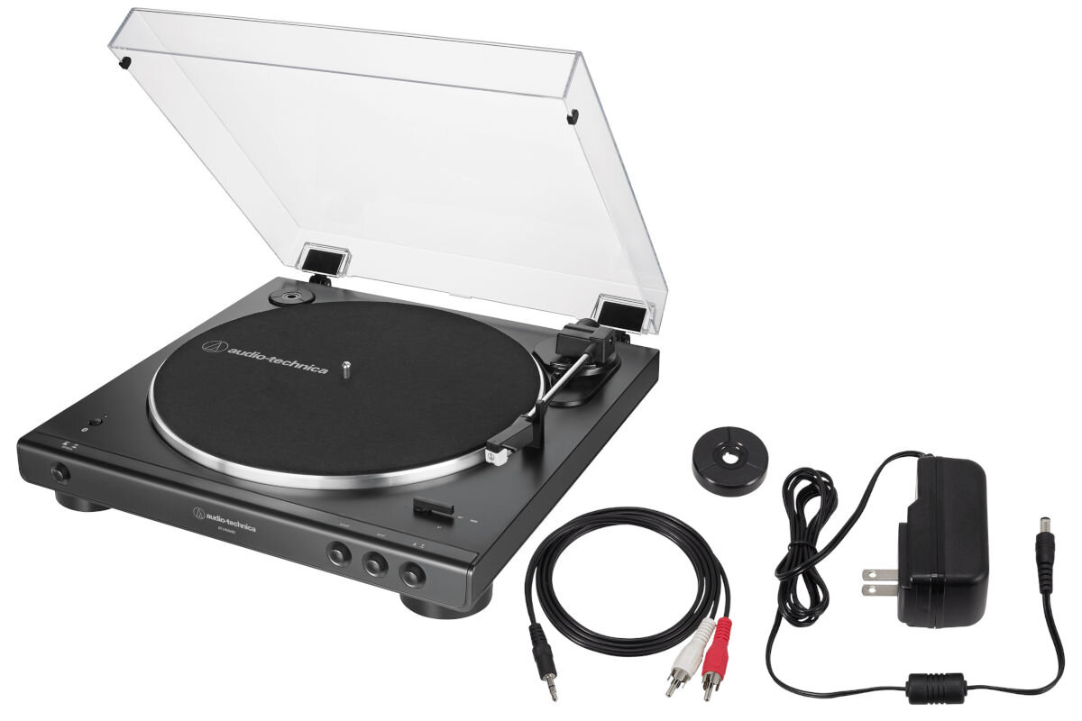 Na obrazie widoczny jest czarny gramofon z przezroczystą pokrywą, obok którego znajdują się kable, adapter i zasilacz. Na gramofonie widnieje logo \'audio-technica\'.