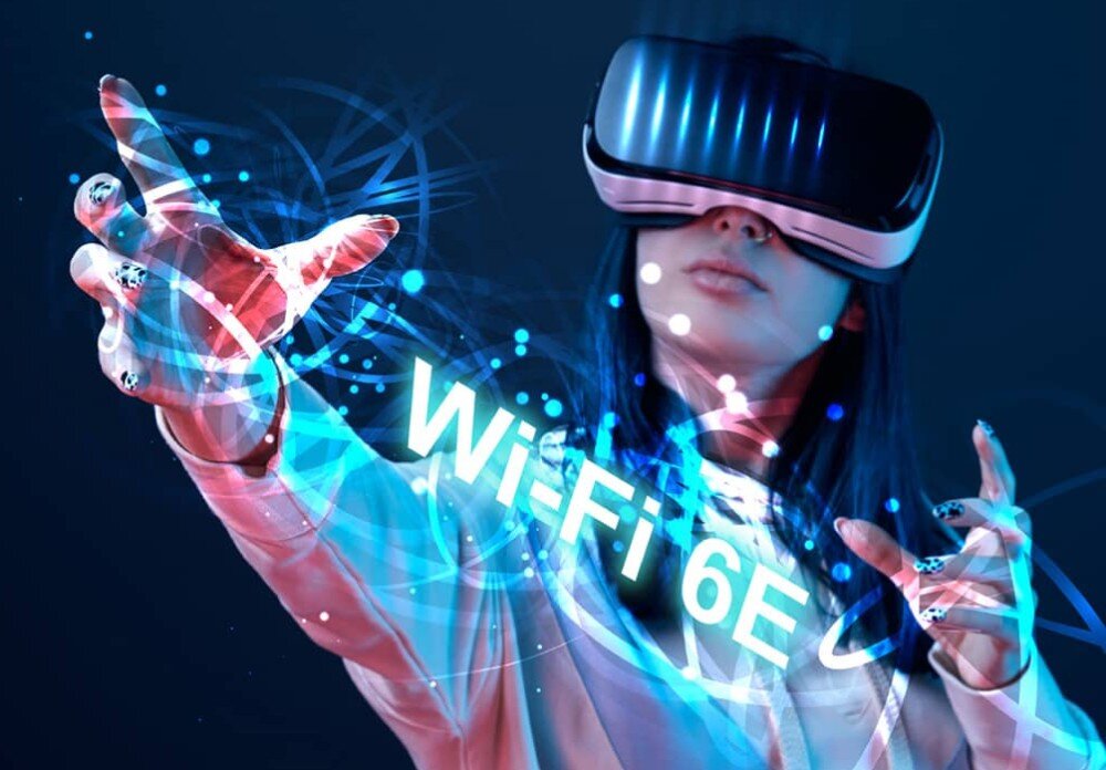 Osoba w okularach VR wyciąga rękę w stronę widza, a wokół niej widoczne są niebieskie efekty świetlne i napis \'Wi-Fi 6E\'.