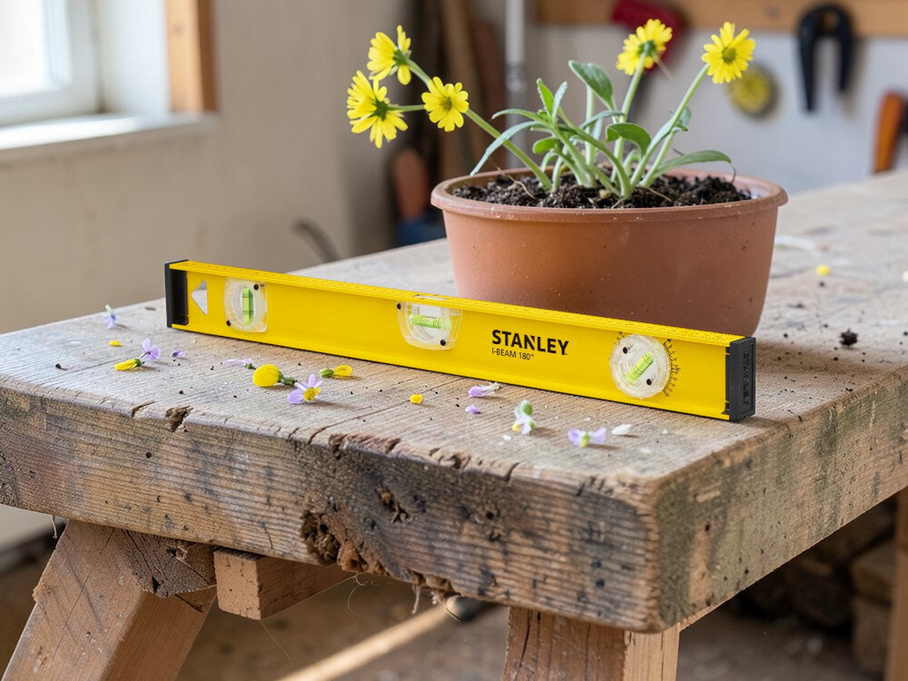 Poziomnica ręczna STANLEY I-Beam 1-42-920, aluminium, korpus, trwałość, waga, Żółta poziomica Stanley leżąca na drewnianym warsztacie obok kwiatów w doniczce.