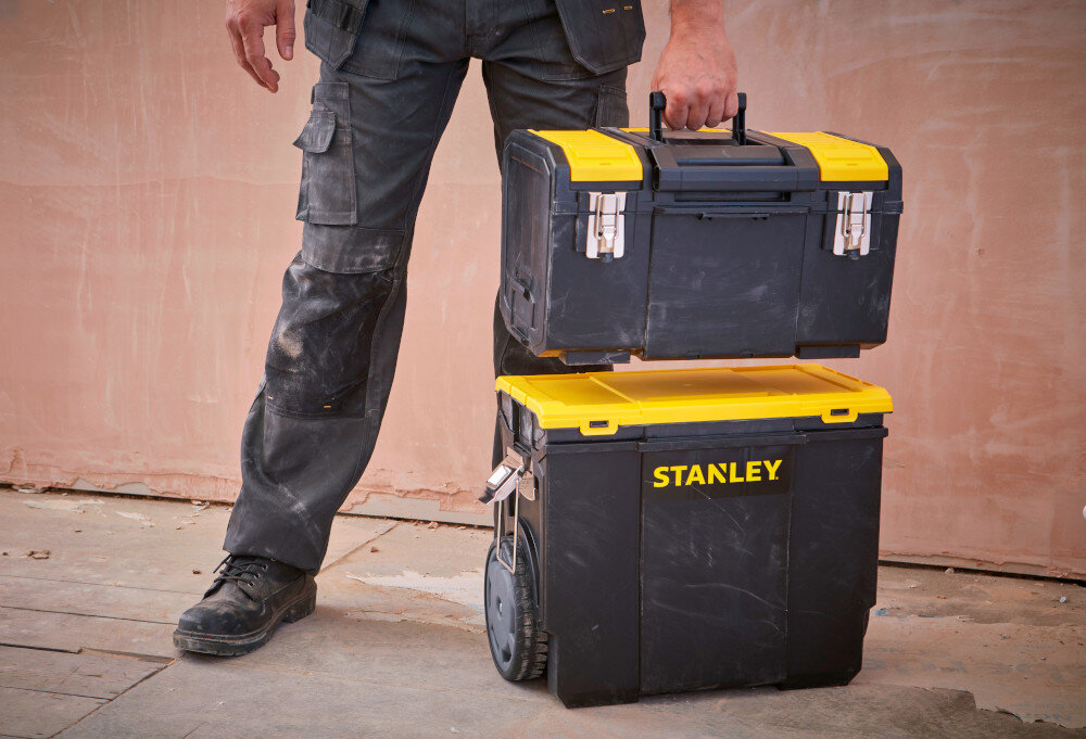 Skrzynka narzędziowa STANLEY 1-70-326 pomieszczenie skrzyni ustawione na podłodze osoba podnosi górną skrzynkę w tle ściana organizacja narzędzi transport przechowywanie mobilność