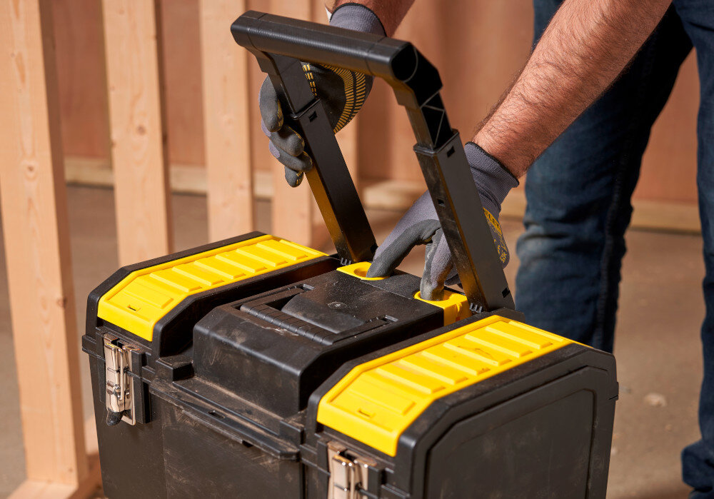 Skrzynka narzędziowa STANLEY 1-70-326 zbliżenie na uchwyt osoba składa uchwyt w tle drewniana ściana teleskopowy uchwyt wygodne manewrowanie przemieszczanie Uchwyty na górze w dolnej części różne opcje przenoszenia