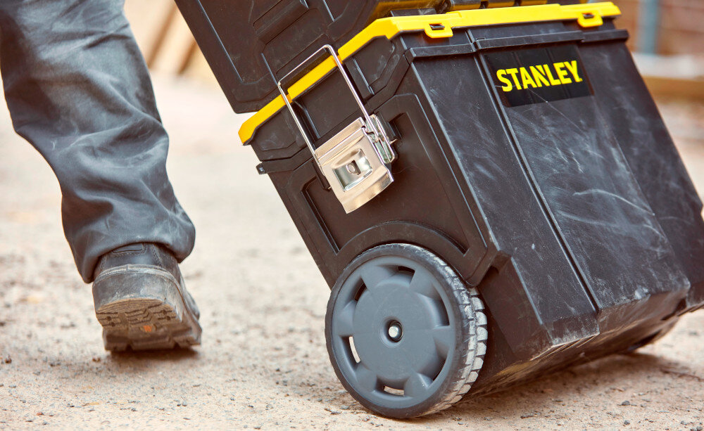 Skrzynka narzędziowa STANLEY 1-70-326 plac budowy osoba ciągnie skrzynki po drodze zbliżenie na koło 7-calowe koła stabilność ułatwiają przemieszczanie solidny układ jezdny