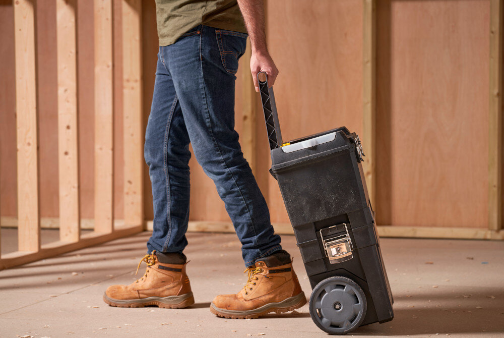 Skrzynka narzędziowa STANLEY 1-93-968 pomieszczenie osoba ciągnie za sobą skrzynki po podłodze trzyma za uchwyt w tle drewniana ściana przemyślana budowa funkcjonalne rozwiązania mobilność pojemność do 55,1 l trwałość usprawnia codzienne obowiązki