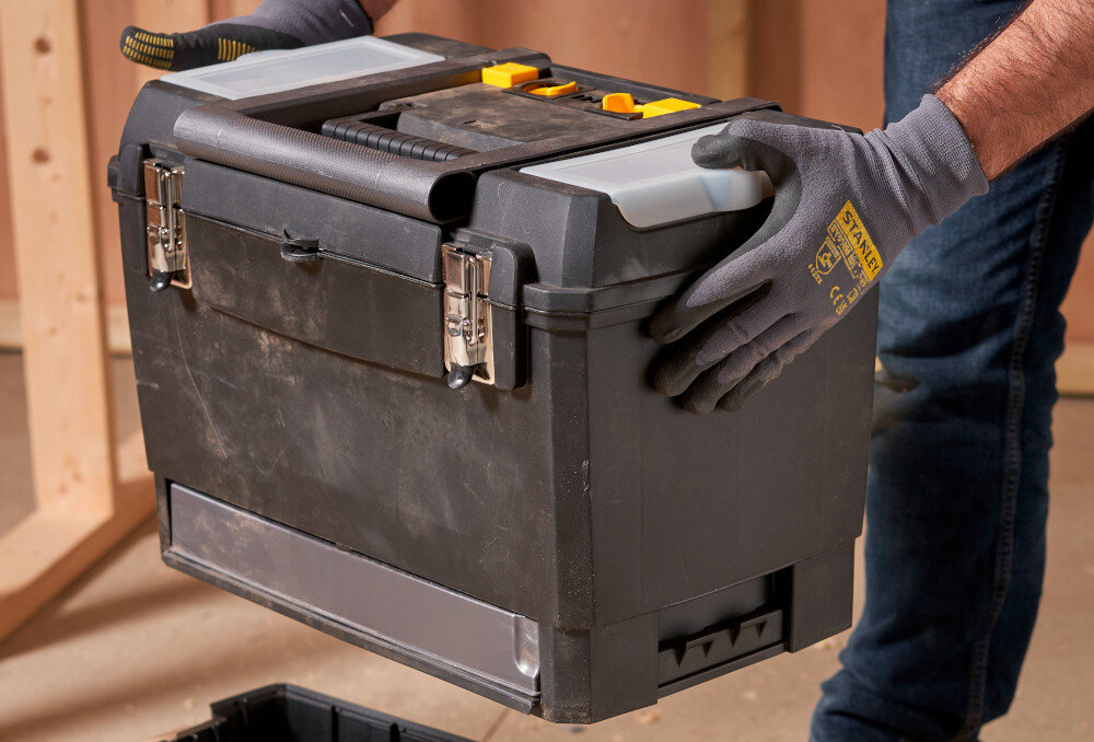 Skrzynka narzędziowa STANLEY 1-93-968 pomieszczenie osoba unosi górną skrzynkę w tle drewniana ściana ergonomiczny uchwyt w górnej części przenoszenie modułu jedną ręką modułowy system ułatwia przenoszenie