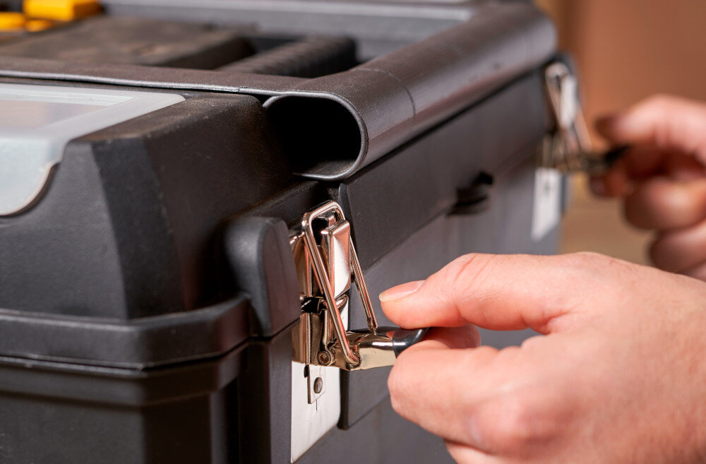 Skrzynka narzędziowa STANLEY 1-93-968 zbliżenie na zatrzaski osoba trzyma zatrzaski w dłoniach metalowe zatrzaski mocne domknięcie skrzynki wymiary 619 × 473 × 295 mm waga około 4,5 kg stabilność w trakcie przenoszenia ogranicza ryzyko przewrócenia się zestawu