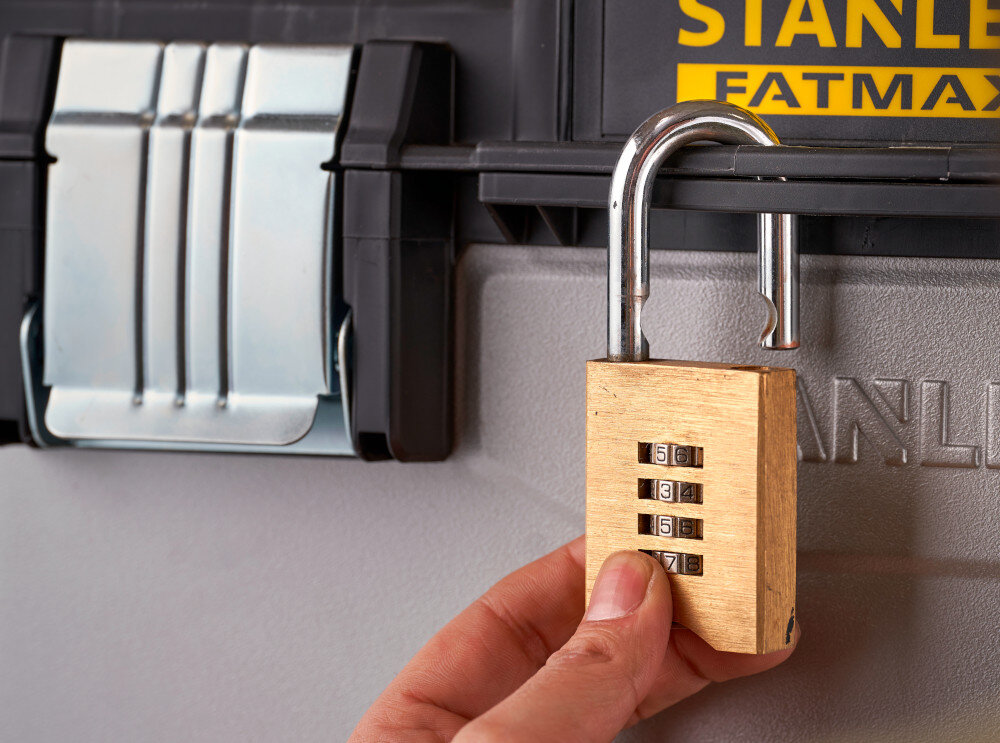 Skrzynka narzędziowa STANLEY FatMax 1-95-622 zbliżenie na otwór do montażu kłódki osoba zakłada kłódkę na skrzynkę możliwość zamknięcia na kłódkę bezpieczeństwo przechowywanych narzędzi cenne akcesoria są dobrze chronione