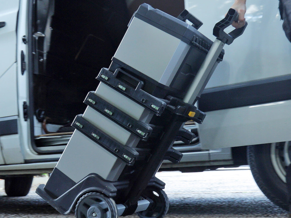 Skrzynka narzędziowa STANLEY FatMax 1-95-622 osoba ciągnie za sobą skrzynki w tle samochód z metalu odpornego tworzywa sztucznego trwałość stabilność metalowe zawiasy metalowa zatrzaski uchwyt typu Bi-Materiał ochrona przed uszkodzeniami mechanicznymi działaniem czynników zewnętrznych