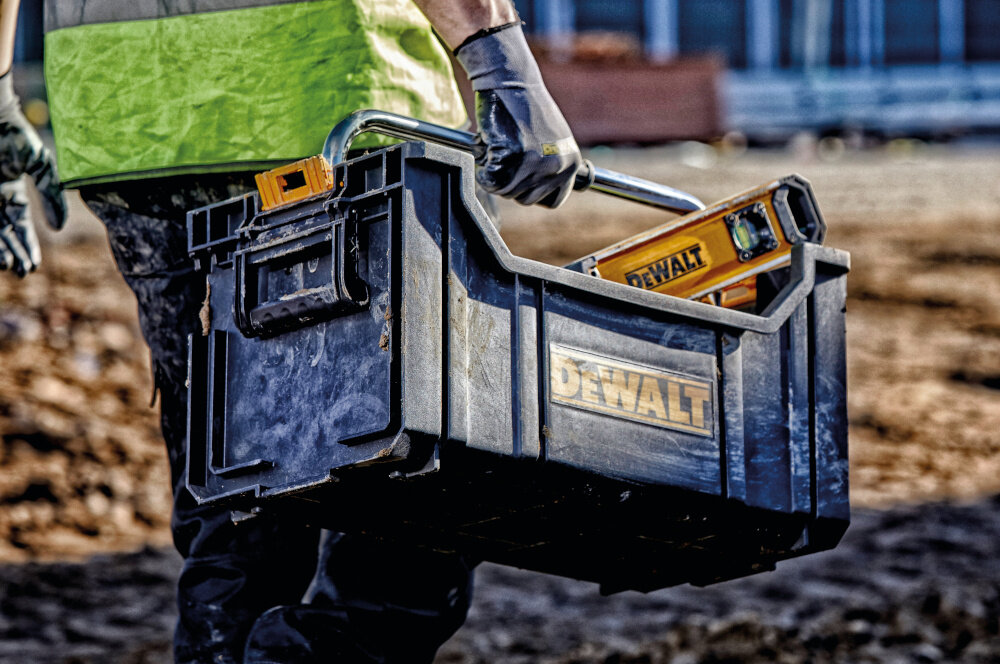 Skrzynka narzędziowa DEWALT DWST1-75654 plac budowy osoba niesie skrzynkę w dłoni skrzynka wypełniona narzędziami organizacja narzędzi duża pojemność komfort przenoszenia sprzętu