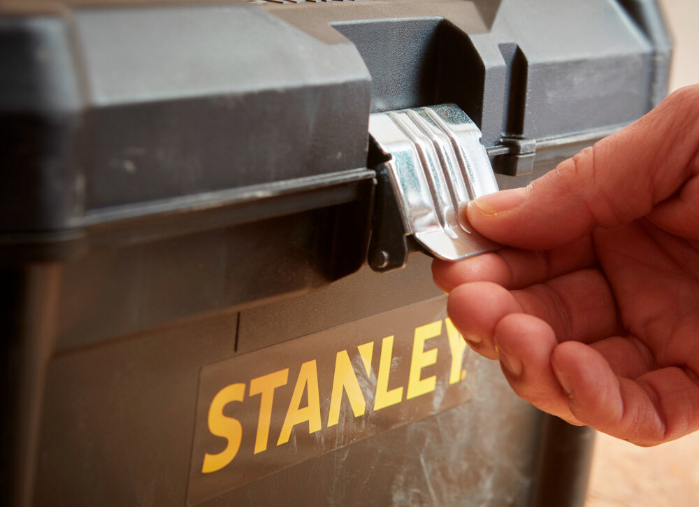 Skrzynka narzędziowa STANLEY STST1-75518 zbliżenie na zamek osoba trzyma zamek w palcach solidny metalowy zamek bezpieczne przechowywanie narzędzi i akcesoriów ochrona zawartość przed przypadkowym otwarciem trwałość