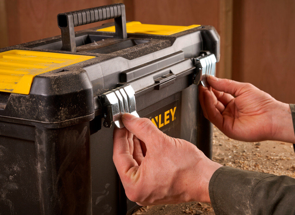 Skrzynka narzędziowa STANLEY Essential STST1-75521 zbliżenie na zamki osoba trzyma zamki w palcach dwa solidne metalowe zamki bezpieczne przechowywanie narzędzi i akcesoriów ochrona zawartość przed przypadkowym otwarciem trwałość
