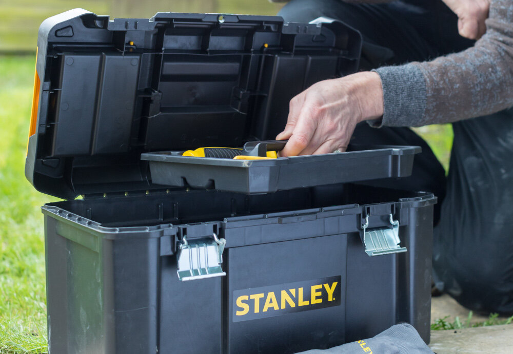 Skrzynka narzędziowa STANLEY Essential STST1-75521 skrzynia wypełniona narzędziami osoba wyciąga ze skrzyni tackę w tle trawa wyjmowana tacka łatwy dostęp ułatwia utrzymanie porządku