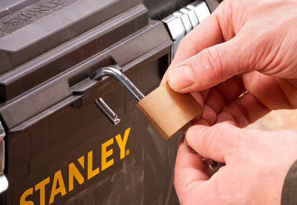 Skrzynka narzędziowa STANLEY Essential STST1-75521 osoba zakłada kłódkę na skrzynię otwór umożliwiający założenie kłódki bezpieczeństwo przechowywanych narzędzi ochrona przed dostępem osób trzecich