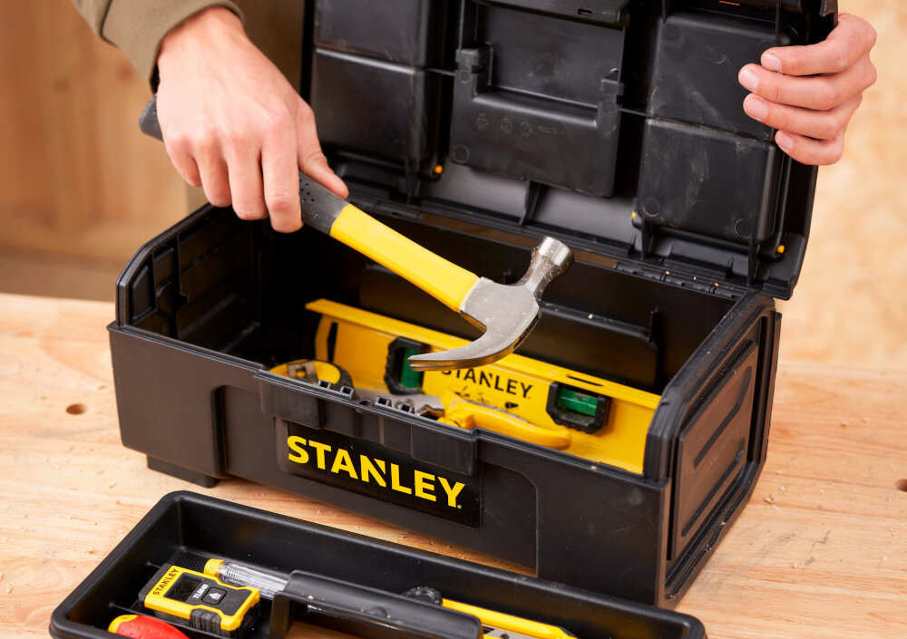 Skrzynka narzędziowa STANLEY Basic 1-79-216 skrzynka na drewnianym blacie obok tacka narzędzia w tle drewniana ściana wygodne przechowywanie narzędzi i akcesoriów porządek w miejscu pracy duża pojemność wnętrza 6,9 litra efektywność komfort