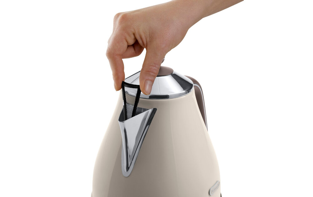 Ręka wyciąga filtr z dzióbka beżowego czajnika z metalowymi elementami. Na czajniku widoczne jest logo \'DeLonghi\'.