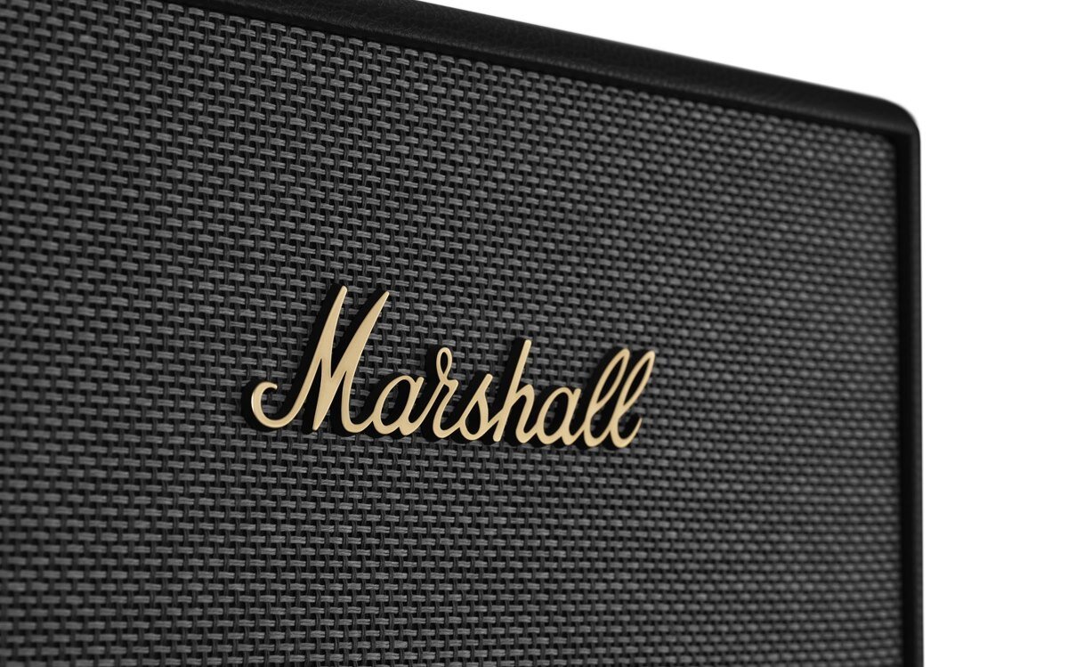 Zbliżenie na czarną kratkę głośnika z widocznym złotym logo \'Marshall\'.