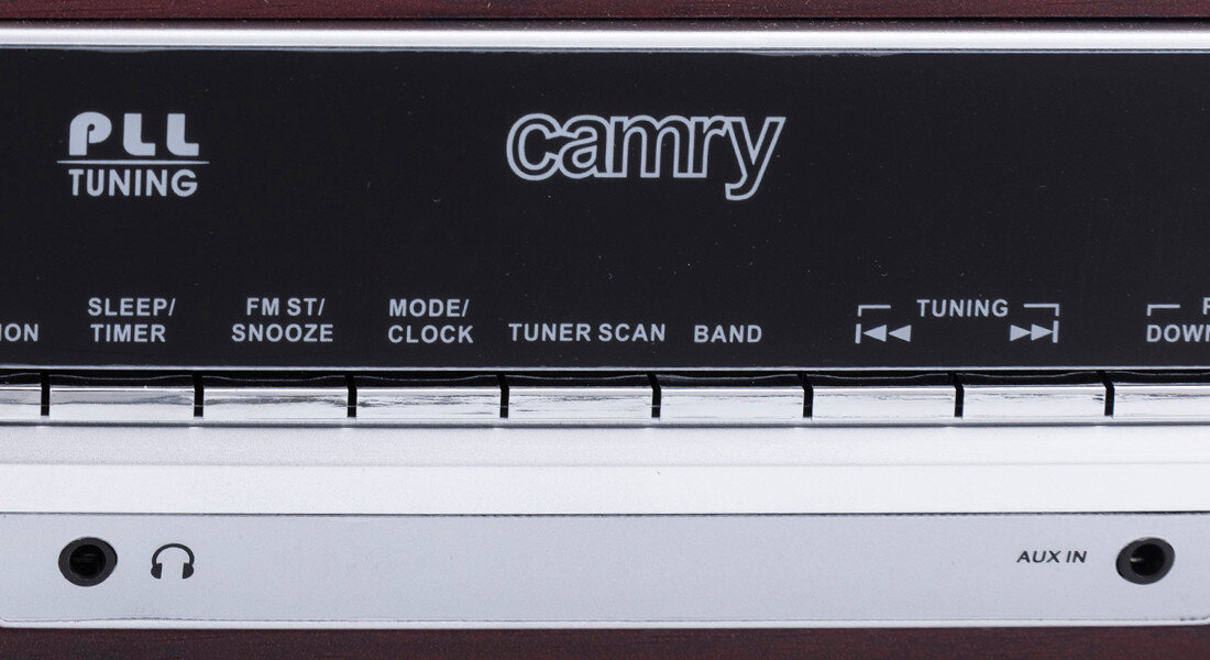 Zbliżenie na panel sterowania urządzenia z widocznym logo \'camry\' oraz napisami: PLL TUNING, SLEEP/TIMER, FM ST/SNOOZE, MODE/CLOCK, TUNER SCAN, BAND. Na dole znajduje się gniazdo słuchawkowe i napis AUX IN.