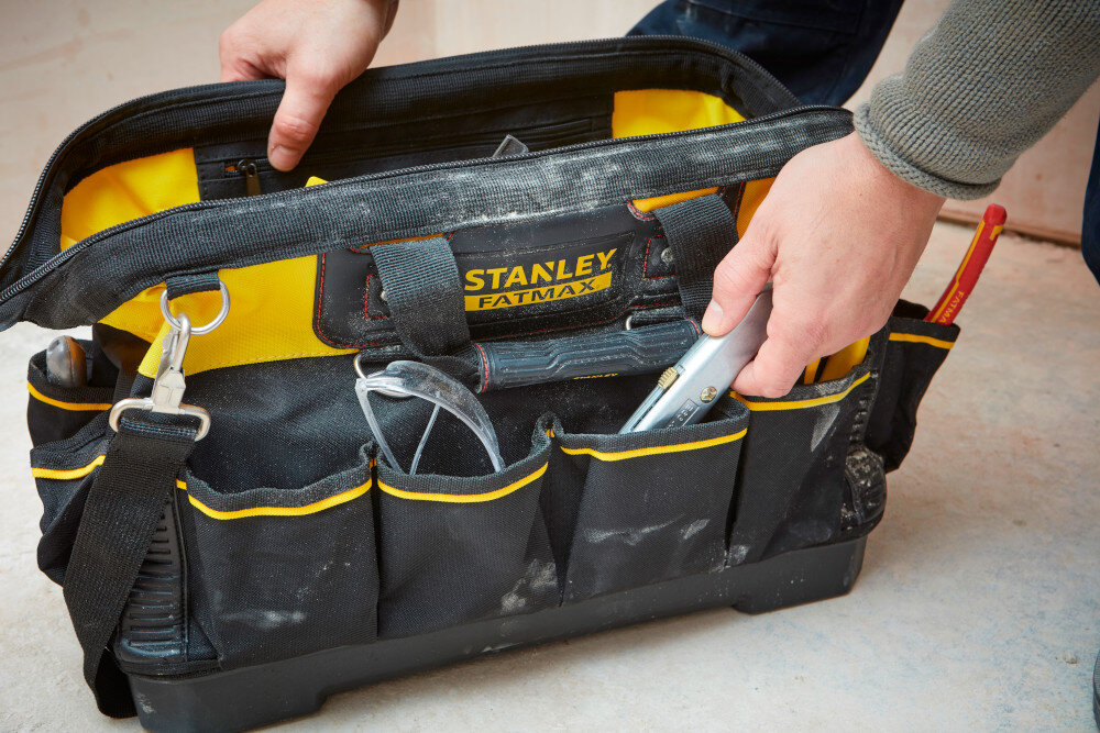 Torba narzędziowa STANLEY 1-93-950 otwarta torba ustawiona na podłodze osoba trzyma ścianki torby w dłoniach duża pojemność do 26,5 litra udźwig do 20 kg wymiary 490 x 260 x 260 mm waga około 1,54 kg solidna konstrukcja mocne dno i praktyczne przegródki