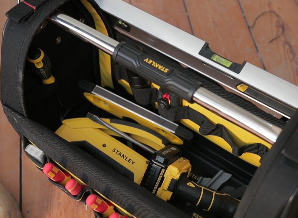 Torba narzędziowa STANLEY Fatmax 1-93-951 pomieszczenie drewniana podłoga widok z góry na torbę wypełnioną narzędziami otwarta budowa natychmiastowe znalezienie odpowiednich narzędzi zintegrowana kieszeń na piłę liczne przegrody boczne akcesoria są rozmieszczone w sposób przejrzysty pojemność do 19 litrów