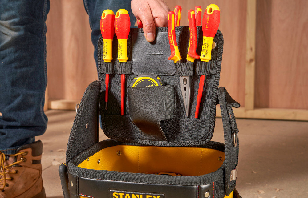 Torba monterska STANLEY Fatmax 1-93-952 pomieszczenie plac budowy drewniana ściana osoba wyciąga z wnętrza kieszeń wypełnioną narzędziami wzmocnione panele boczne stabilność ochrona narzędzi torba nie odkształca się wyjmowana kieszeń przeznaczoną na mniejsze narzędzia