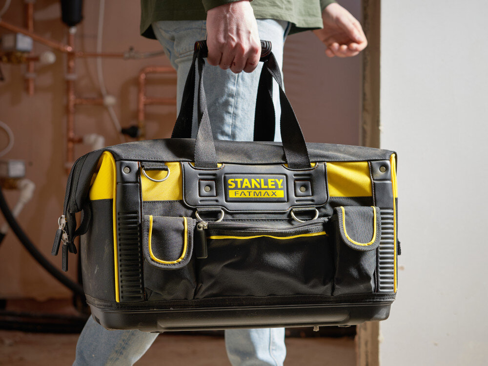Torba narzędziowa STANLEY FMST1-71180 pomieszczenie osoba trzyma torbę w dłoni w tle ściana wykonana z nylonu 600x600 Denier wysoka odporność na przetarcia i rozdarcia wzmocnione szwy dodatkowe nity
