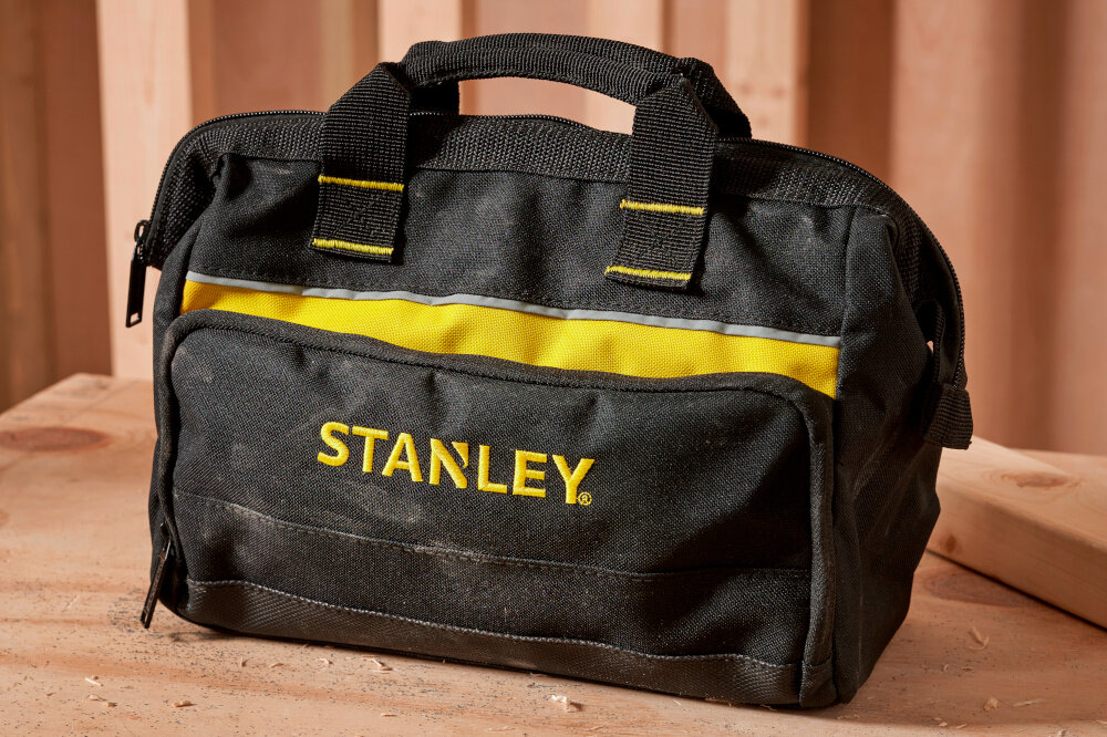 Torba narzędziowa STANLEY 1-93-330 pomieszczenie blat roboczy zamknięta torba ustawiona na blacie w tle drewniana ściana organizacja narzędzi uniwersalne zastosowanie mobilność porządek