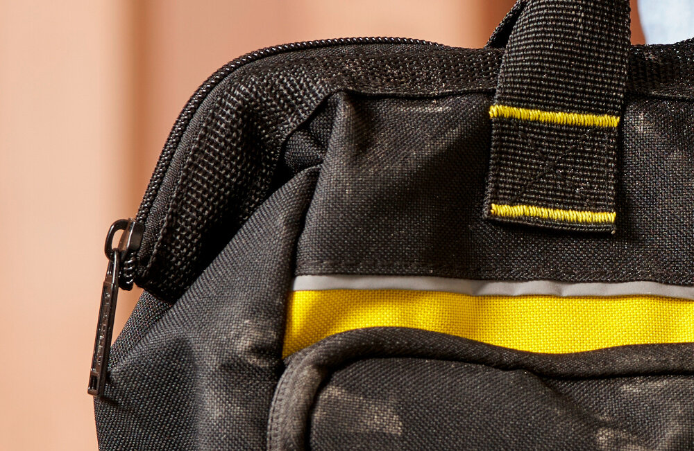 Torba narzędziowa STANLEY 1-93-330 pomieszczenie w tle drewniana ściana zbliżenie na zamek podstawa torby została wzmocniona plastikiem ochrona przed przetarciem i zamoczeniem narzędzia pozostają suche i gotowe do użycia do użytku w trudnych warunkach pracy zamek błyskawiczny