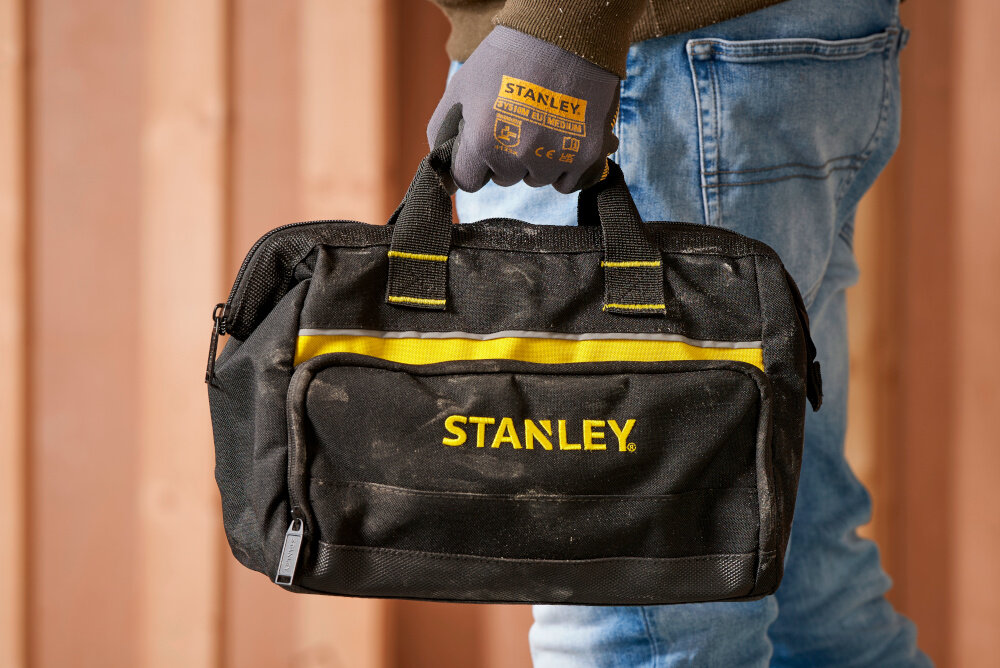 Torba narzędziowa STANLEY 1-93-330 pomieszczenie osoba niesie torbę w dłoni w tle drewniana ściana waga około 0,45 kg lekka i poręczna uchwyt do przenoszenia pasek na ramię