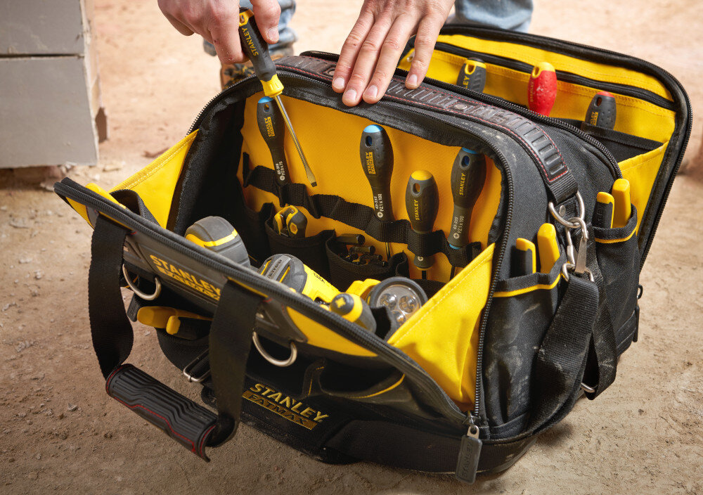 Torba narzędziowa STANLEY Fat Max FMST1-73607 plac budowy otwarta torba ustawiona na podłodze osoba wyciąga z wnętrza śrubokręt do przechowywania i transportu narzędzi duża pojemność przemyślana organizacja przestrzeni do użytku w warsztacie i w terenie