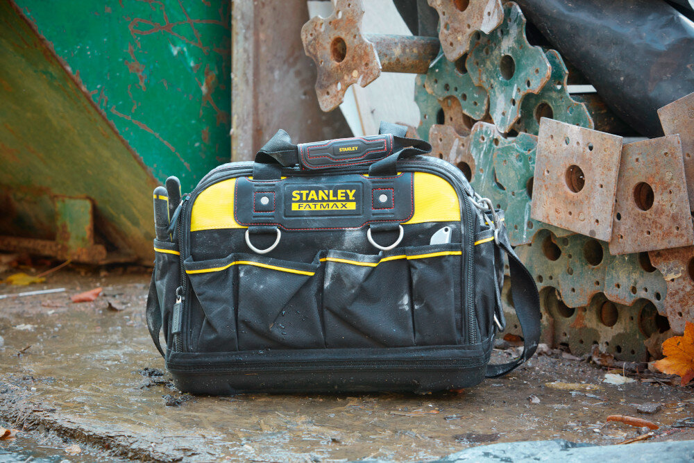 Torba narzędziowa STANLEY Fat Max FMST1-73607 plac budowy torba ustawiona na mokrym podłożu w tle metalowe konstrukcje i elementy dno wykonano z wytrzymałego wodoodpornego tworzywa ochrona przed wilgocią i zabrudzeniami usztywnione panele stabilny kształt