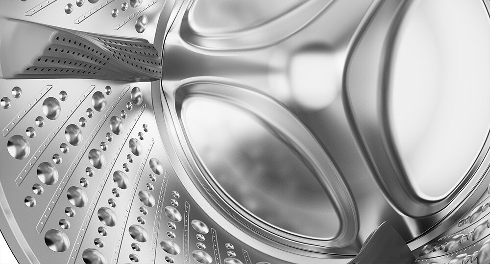 Zbliżenie na wnętrze bębna pralki z metaliczną powierzchnią i otworami wentylacyjnymi. Struktura bębna jest gładka i lśniąca.