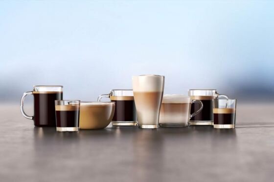 Na obrazie znajduje się siedem szklanek z różnymi rodzajami kawy, w tym espresso, cappuccino i latte. Tło jest rozmyte, co podkreśla napoje na pierwszym planie.