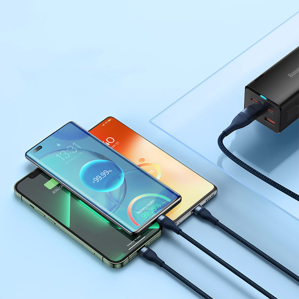 Trzy smartfony są podłączone do czarnej ładowarki za pomocą niebieskich kabli USB. Na ekranach telefonów widoczne są wskaźniki ładowania z wartościami 99,99% i 56%.