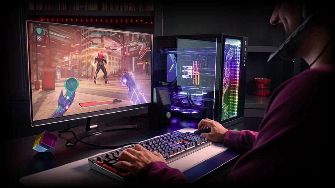 Osoba siedzi przy biurku, grając w grę komputerową na monitorze. Obok znajduje się komputer z podświetleniem RGB i klawiatura mechaniczna.