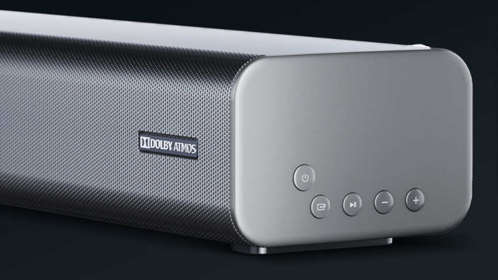Czarny soundbar z widocznym logo \'Dolby Atmos\' na siatce. Na bocznej części znajdują się cztery przyciski: włączania, wyboru źródła, odtwarzania/pauzy oraz regulacji głośności.
