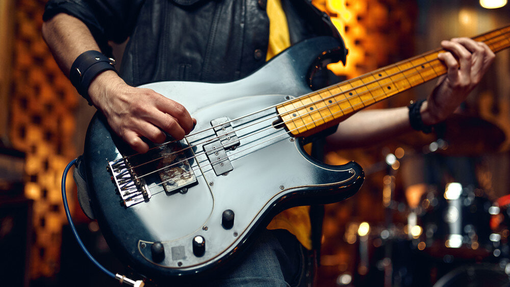 Osoba gra na gitarze basowej w pomieszczeniu z rozmytym tłem. Instrument ma jasnoniebieski korpus i metalowe elementy.
