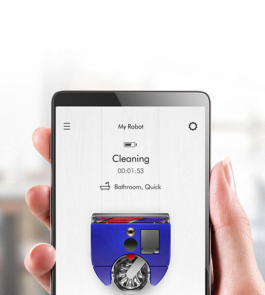 Osoba trzyma smartfon z aplikacją pokazującą status robota sprzątającego. Na ekranie widnieje tekst: \'My Robot\', \'Cleaning 00:01:53\', \'Bathroom, Quick\'.