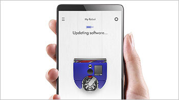 Osoba trzyma smartfon, na którym wyświetla się ekran aplikacji z napisem \'Updating software...\' oraz obrazem robota sprzątającego w kolorze niebieskim.